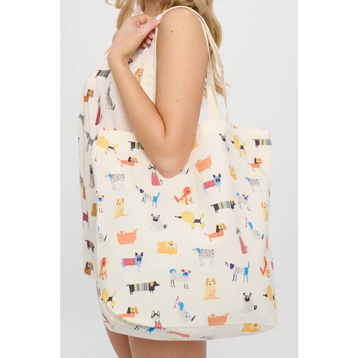 Close-up of a model holding a tote bag with a whimsical dog pattern, showcasing playful, detailed illustrations of dogs against a light background.