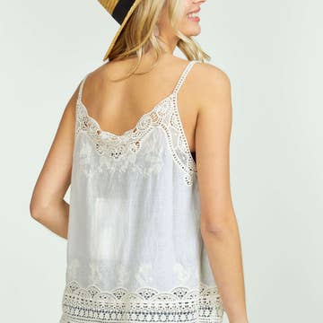 Back view of a woman in an embroidered crochet tank top and denim shorts, wearing a straw hat.
