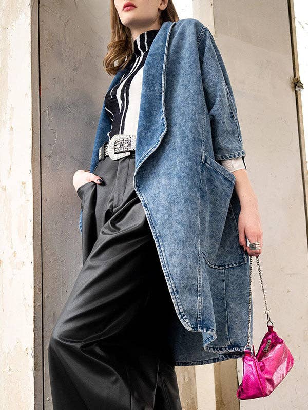 Oversized denim jacket with 3/4 sleeves and large pockets, offering a relaxed fit and stylishly casual vibe. Paired with a striped turle neck, black trousers, and neon pink handbag.
