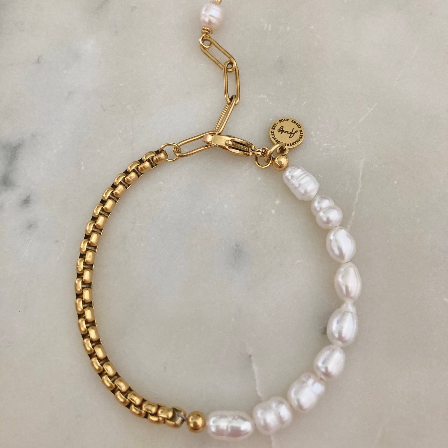 Close-up of a pearl bracelet with a gold-plated box chain, displayed on a marble surface.