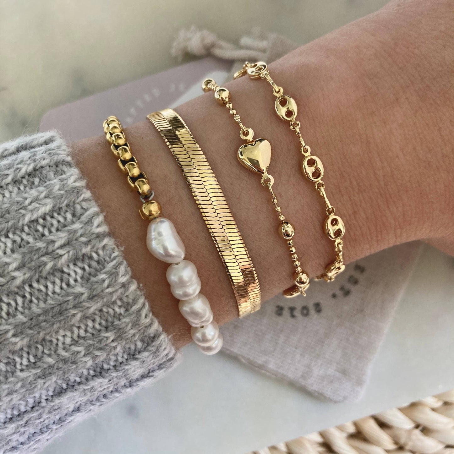Wrist adorned with multiple bracelets, including a pearl bracelet with a gold-plated box chain.