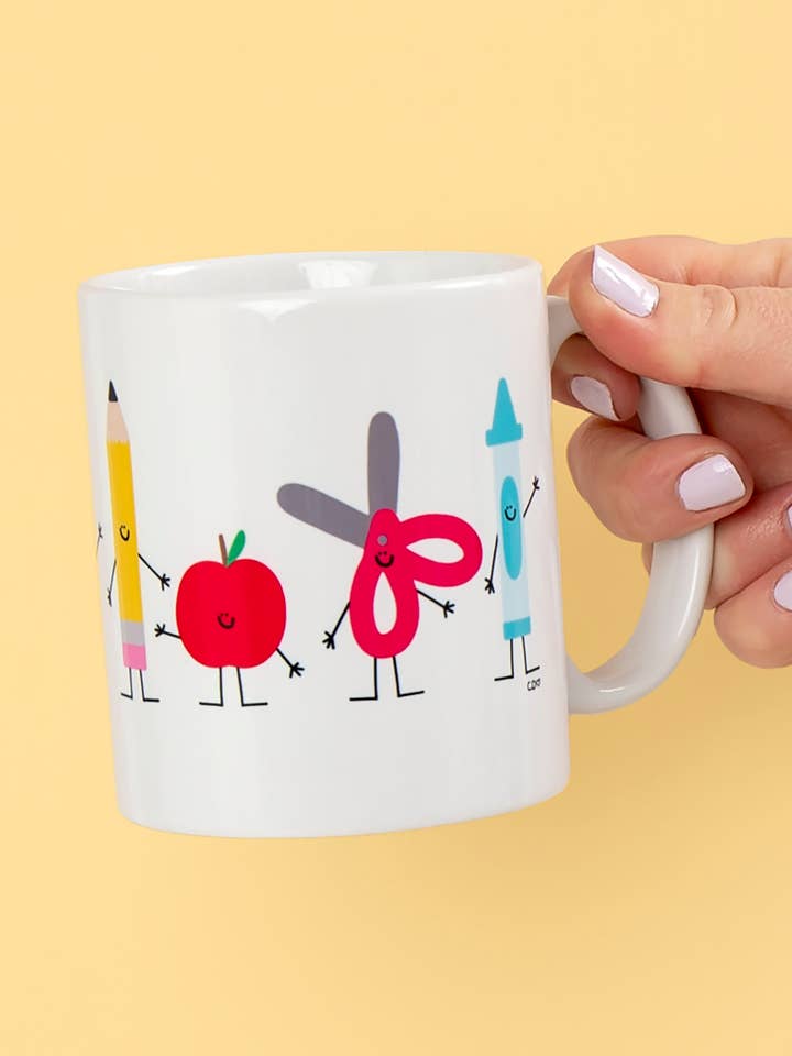 White mug featuring a line of personified school supplies, including smiling pencils, rulers, notebooks, and more.
