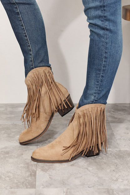 Side view of model wearing stylish ankle boots featuring fringe detailing, embodying cowboy-inspired fashion. With a point toe and high heel height of 2 inches, these boots blend rugged charm and feminine elegance. Imported and designed for a modern twist on the classic cowboy look, they are a versatile addition to any wardrobe.