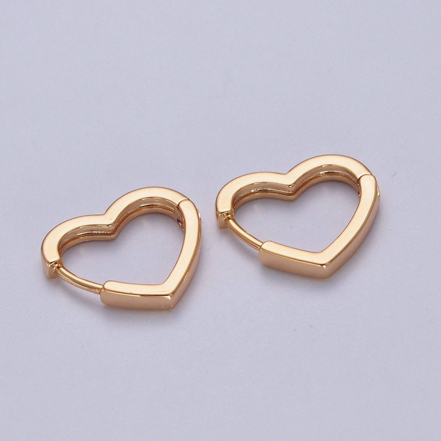 Pair of 24K gold-filled heart-shaped huggie hoop earrings on a white background.