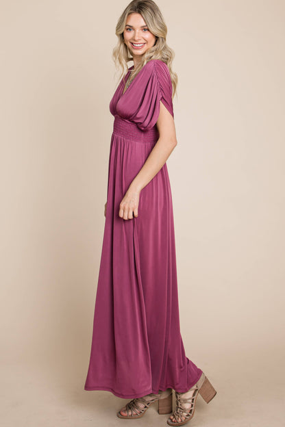 Woman in maxi Grape dress, side view, smiling and looking at the camera.