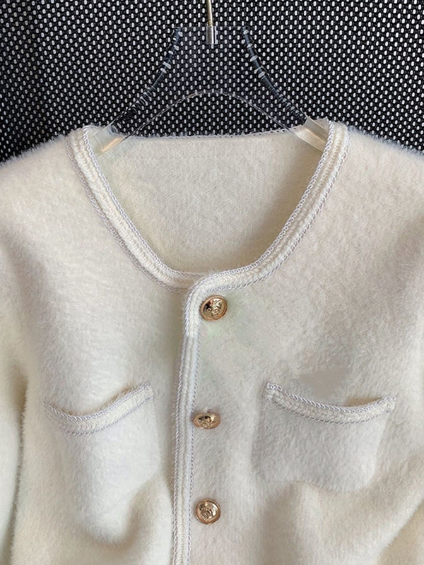 Close-up view of a golden embossed button on a white velvet cardigan, showcasing intricate details and soft velvet fabric.