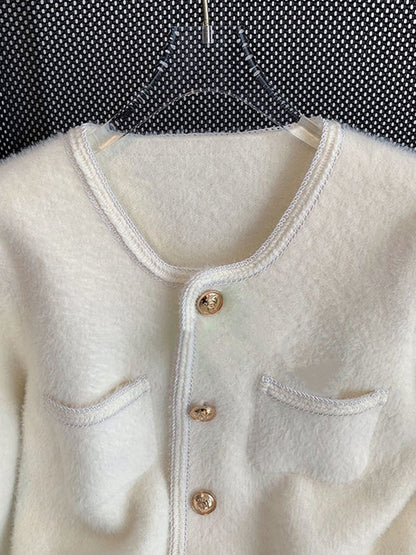 Close-up view of a golden embossed button on a white velvet cardigan, showcasing intricate details and soft velvet fabric.