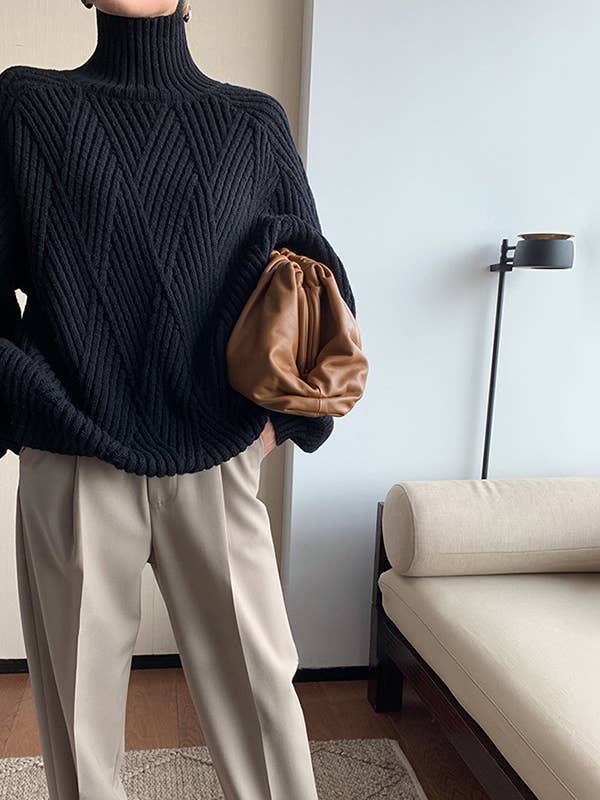 Woman wearing a black turtle neck long sleeve pullover sweater with beige trousers, holding a brown clutch.