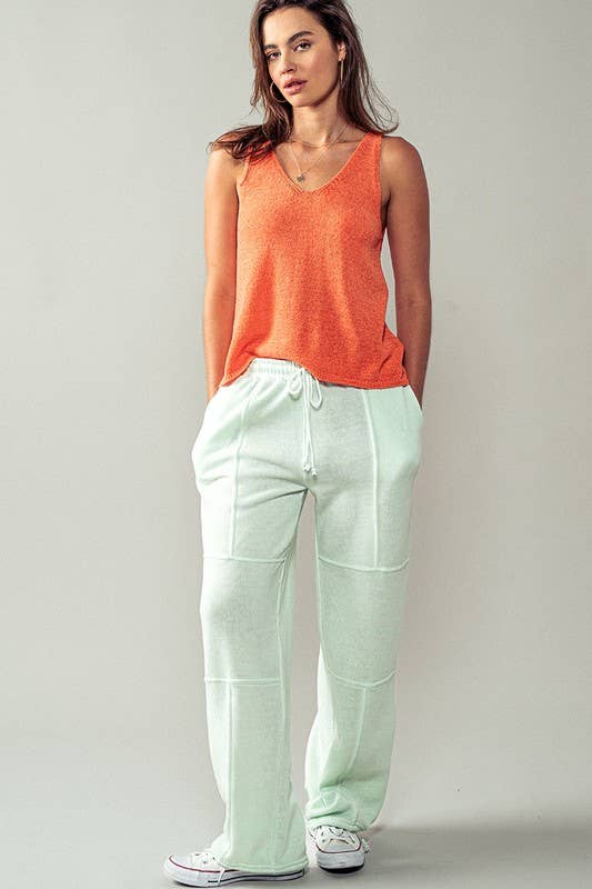 Model standing in an orange knitted tank top and white drawstring pants, showing a full-body view of a relaxed summer outfit.