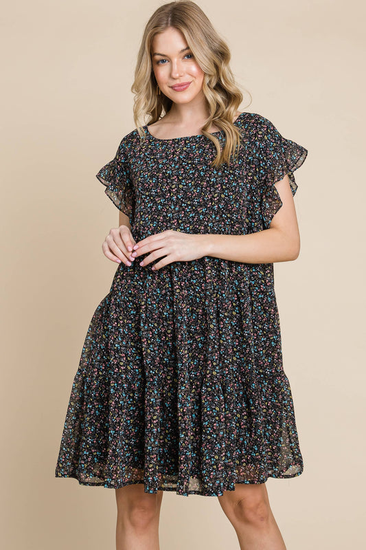 Front view of a woman wearing a black floral print dress with ruffle sleeves, standing with hands together.