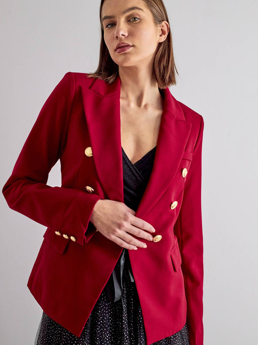 Woman wearing a black fitted blazer with gold buttons over a zebra print top, posing against a stone wall.