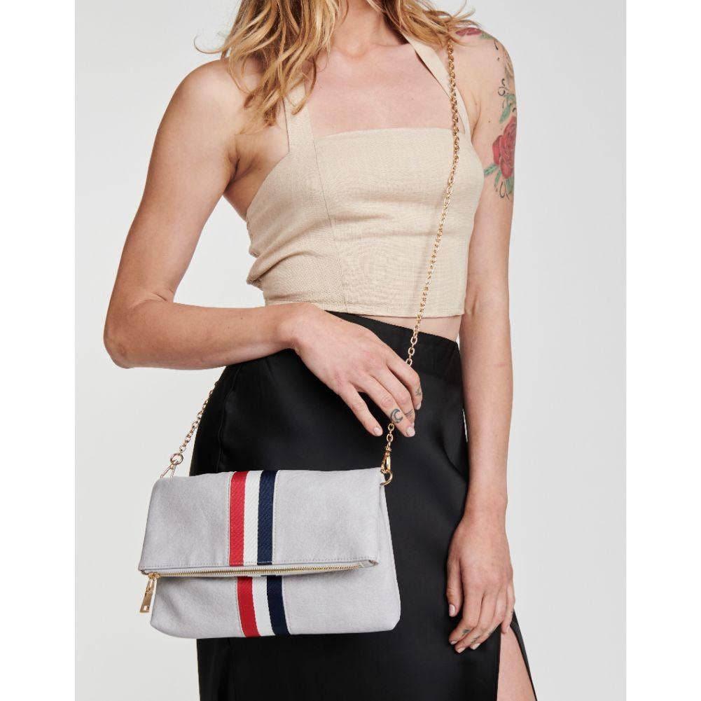 Model wearing a beige top and black skirt, holding the gray fold-over clutch with a red, white, and blue stripe as a crossbody bag with a gold chain strap.