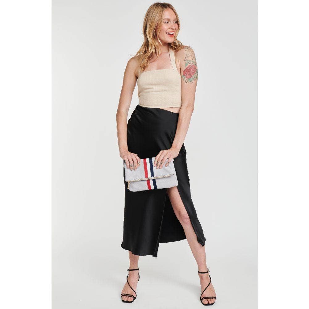 Model in a beige top and black skirt, holding the gray fold-over clutch with a red, white, and blue stripe, smiling and showcasing a chic outfit idea.