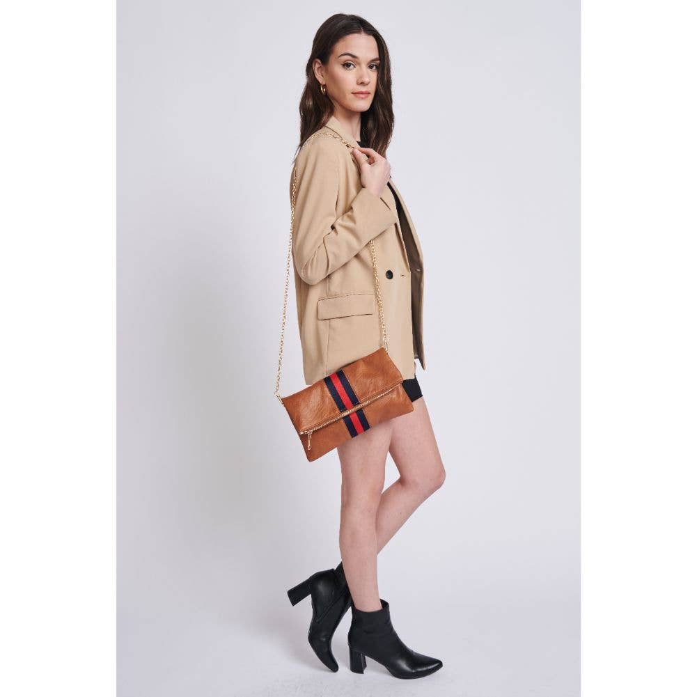 Model wearing a beige blazer and black dress, holding a brown fold-over clutch with a red and navy stripe, featuring a gold chain strap.