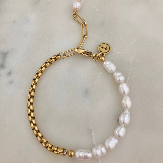 Close-up of a pearl bracelet with a gold-plated box chain, displayed on a marble surface.