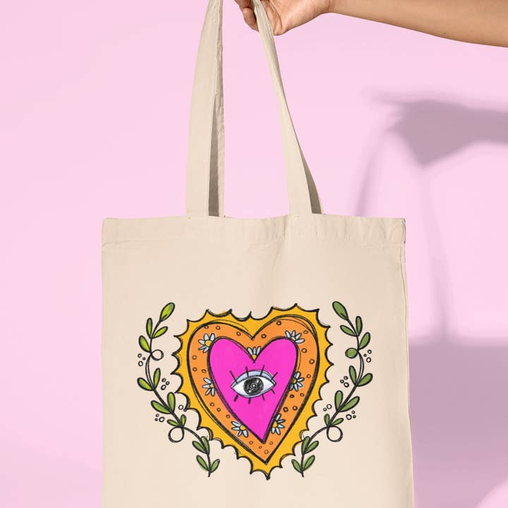 A vibrant tote bag featuring a bold, colorful Sacred Heart design. The heart is surrounded by intricate floral patterns, radiating warmth and positive energy. This spacious and stylish tote is perfect for teachers on the go, adding a meaningful and artistic touch to any outfit.