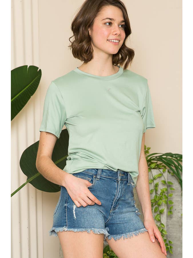 A woman wearing a light green short-sleeve top and denim shorts, smiling and looking to the side.