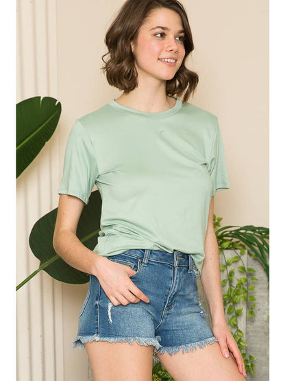 A woman wearing a light green short-sleeve top and denim shorts, smiling and looking to the side.