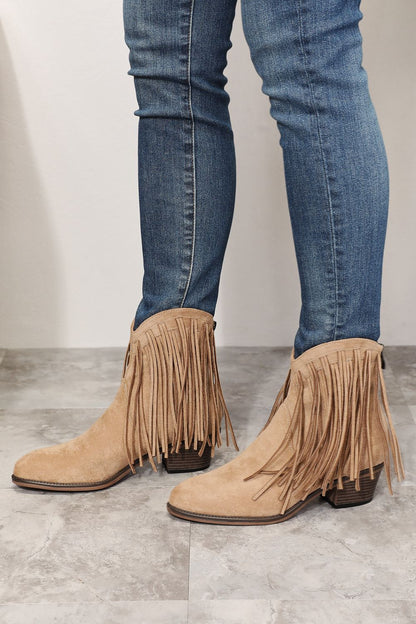 Side view of model wearing stylish ankle boots featuring fringe detailing, embodying cowboy-inspired fashion. With a point toe and high heel height of 2 inches, these boots blend rugged charm and feminine elegance. Imported and designed for a modern twist on the classic cowboy look, they are a versatile addition to any wardrobe.